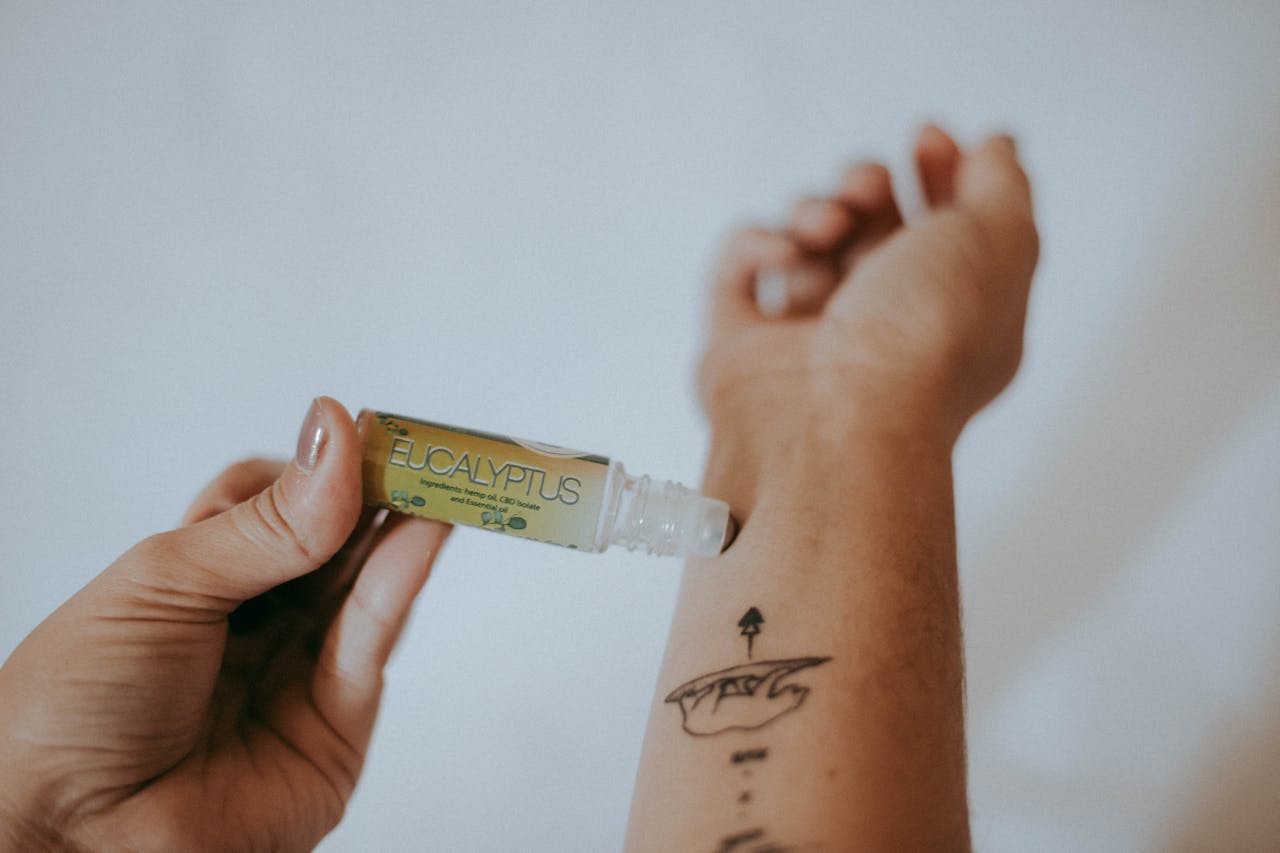 Hand applying Eucalyptus CBD roller oil to tattooed wrist, small roll-on bottle with green label visible.